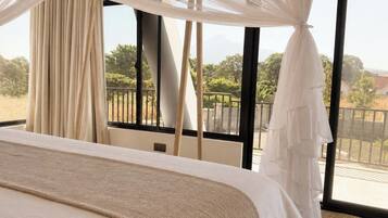 Un dormitorio con una cama grande, cortinas translúcidas y vistas al exterior.