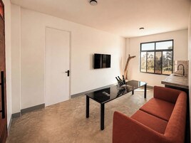 Una sala moderna con sofá, una mesa de centro, televisor montado en la pared y ventana con vistas al exterior.