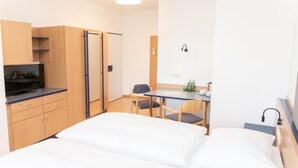 Una habitación de hotel con cama, escritorio, silla, televisor y armario.