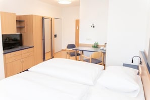 Una habitación de hotel con cama, escritorio, silla, televisor y armario.