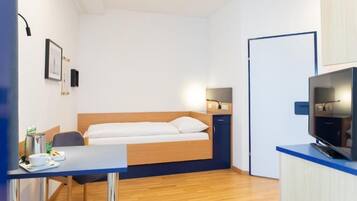 A compact hotel room with a bed, a desk with a chair, a television, and a small cabinet.