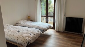 Een slaapkamer met twee bedden, een nachtkastje, een lamp, een raam met gordijnen en een radiator.