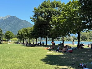 Ein Park mit grünen Wiesen, Bäumen und einem See, im Hintergrund Berge.