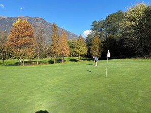 Ein Golfplatz mit Fahnenstange, Bäumen und Bergen im Hintergrund.