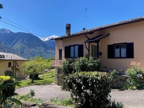 Ein zweistöckiges Haus mit Balkon, Blick auf die Berge und einer Steinmauer im Vordergrund.