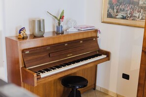 A wooden piano with a bench, a vase with a plant, and a framed picture on the wall. - An entire house made of stone and wood, surrounded by greenery (Bagnolo Piemonte)