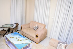 Un salon avec un canapé beige, une table basse en verre, des fauteuils en osier et un tapis à motifs.
