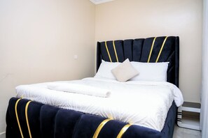 A bed with a dark headboard and white bedding, a white pillow, and a rolled white towel. - Modern 1 Bedroom Apartment in Utawala  Free Wi-Fi & Parking (Nairobi)