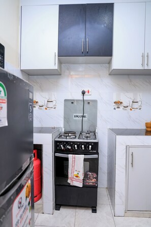 A compact kitchen with a gas stove, white cabinets, and a marble backsplash. - Modern 1 Bedroom Apartment in Utawala  Free Wi-Fi & Parking (Nairobi)