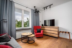 Ein modernes Wohnzimmer mit einem roten Sessel, einer Holzkommode, einem Fernseher und einem Fenster mit Vorhängen.
