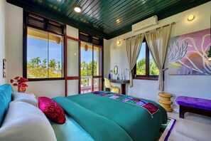 Una habitación con una cama, un banco, una silla, una mesa y un cuadro.