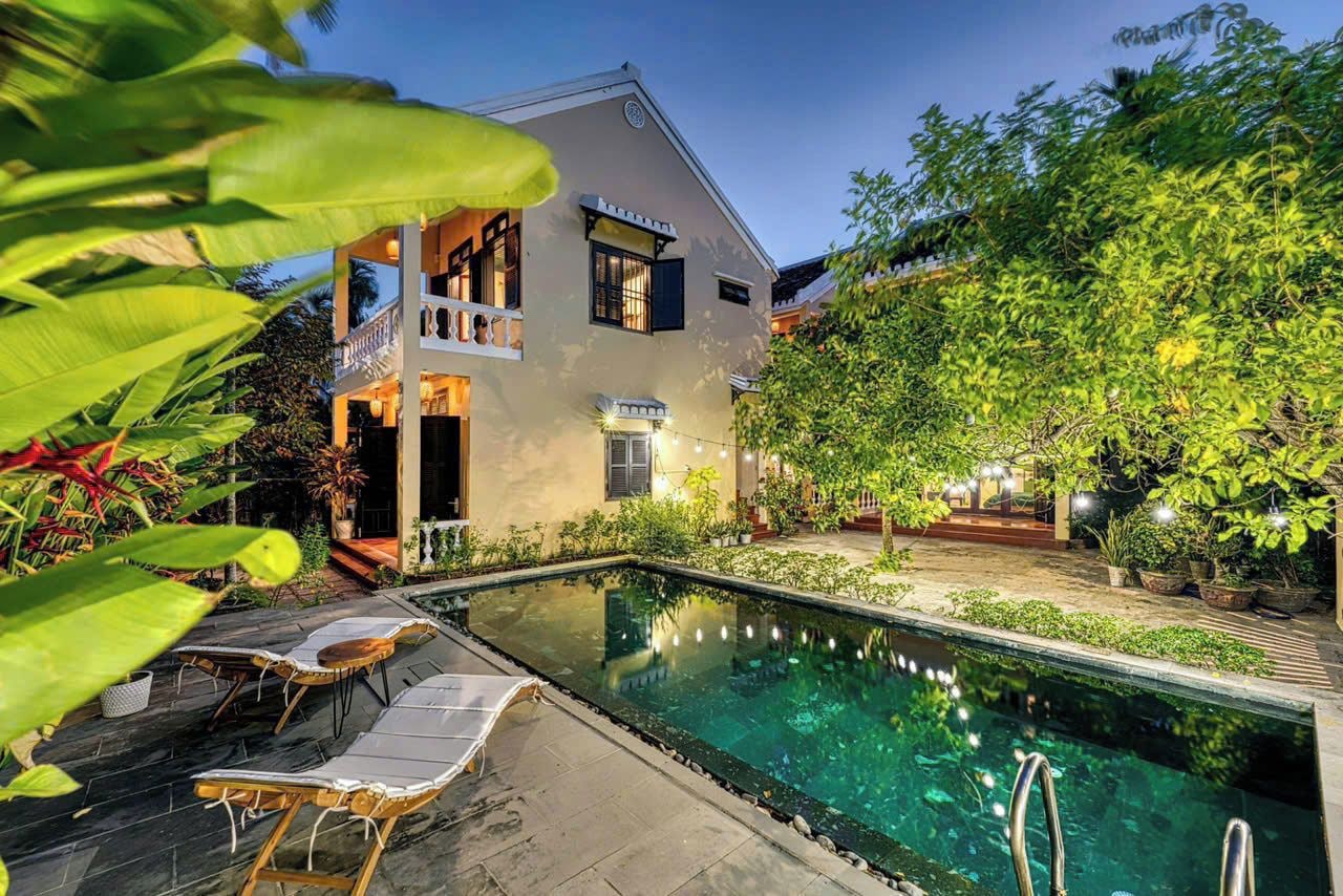 A two-story building with a swimming pool, lounge chairs, and a well-maintained garden.