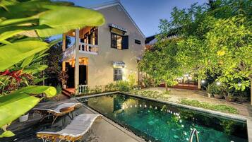 A two-story building with a swimming pool, lounge chairs, and a well-maintained garden.