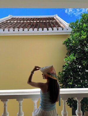 Ein Balkon mit Geländer, eine Person mit Hut und ein Gebäude mit Ziegeldach.