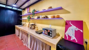 Una cocina con mostrador, estantes con vajilla, microondas y un cuadro.