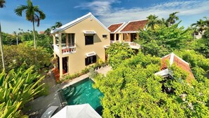 A two-story building with a swimming pool, surrounded by lush greenery and palm trees. - Xao xac Homestay (Da Nang)