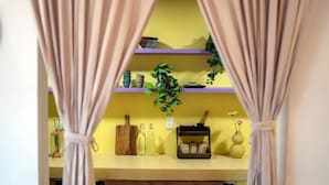 Una cocina con pared amarilla, estantes de madera y una planta colgante.
