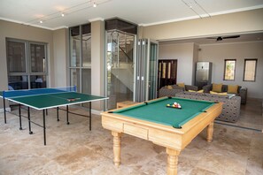 A room with a ping pong table, a pool table, and a sofa with cushions. - Silver Horizon (Knysna)