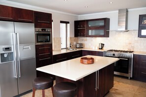 A modern kitchen with stainless steel appliances, dark wood cabinets, and a central island with stools. - Silver Horizon (Knysna)