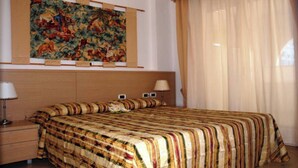 Hotellihuone, jossa on suuri sänky, kaksi yöpöytävalaisinta, yöpöytä ja seinällä oleva seinävaate.
