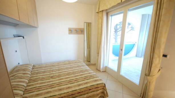 A bedroom with a bed, a window with curtains, and a view of the outside. - Refined flat for unforgettable stays (Bibione)