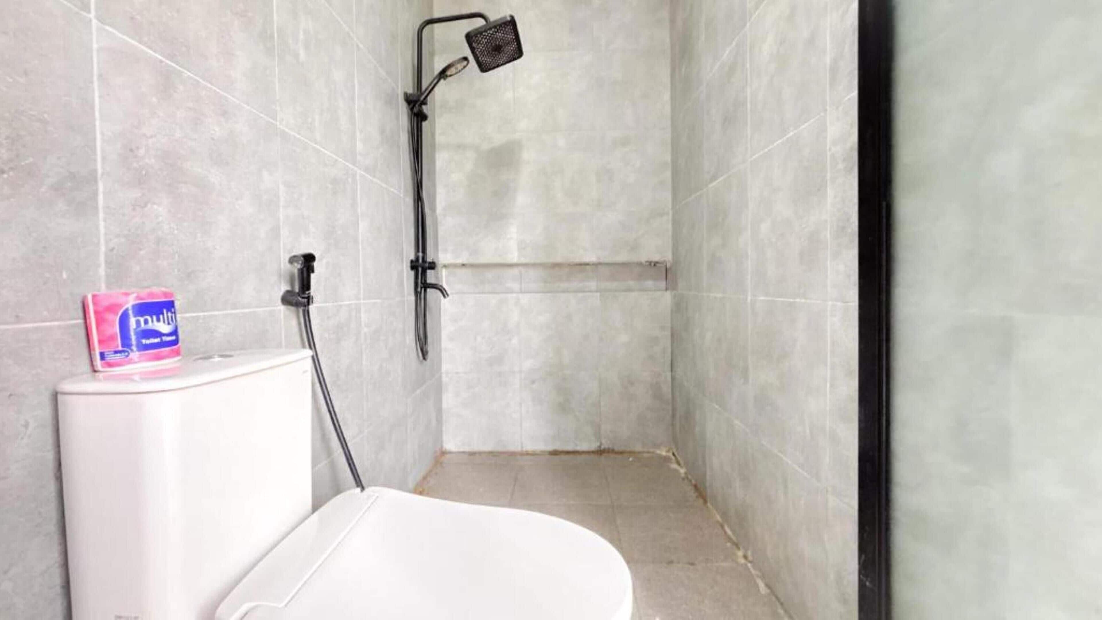 A bathroom with a shower, toilet, and a package of toilet paper on the toilet.