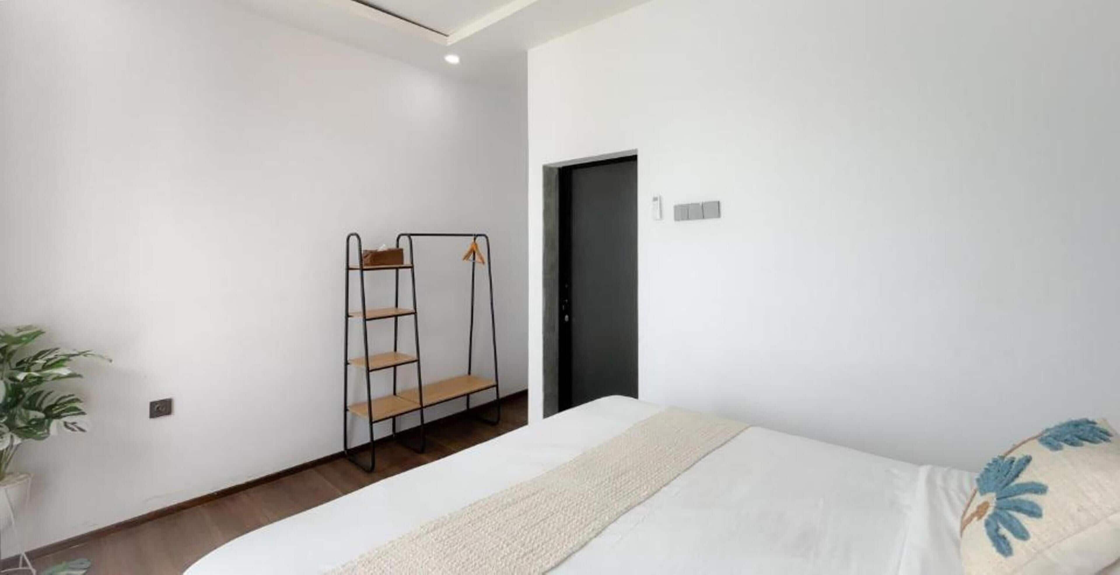 Een slaapkamer met een bed, een houten vloer, een wandplank en een deur.