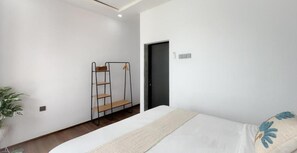 Un dormitorio con cama, piso de madera, estante en la pared y una puerta.