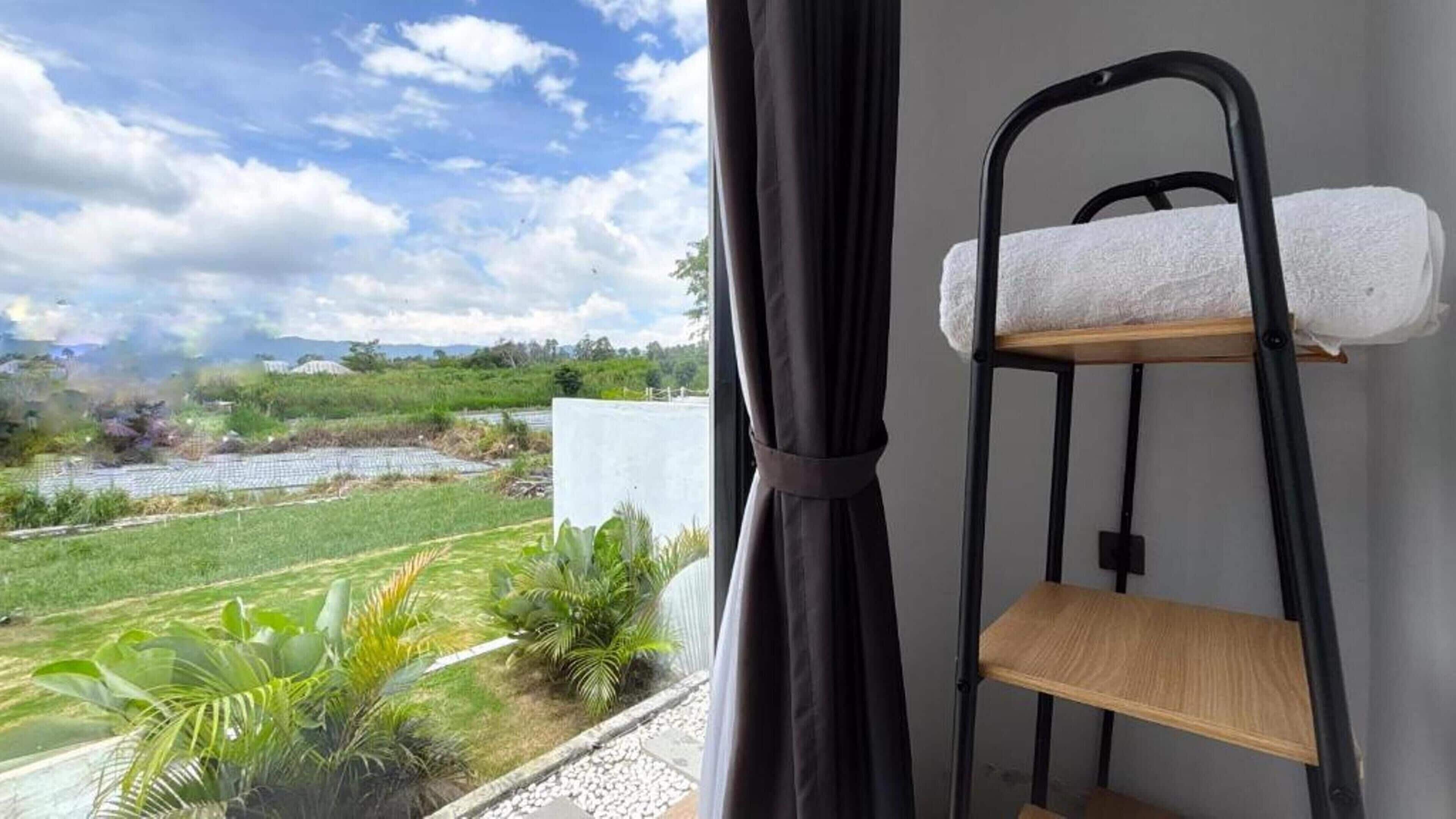 A room with a view of a green landscape and a river, a black metal shelf with a towel, and a curtain partially drawn.