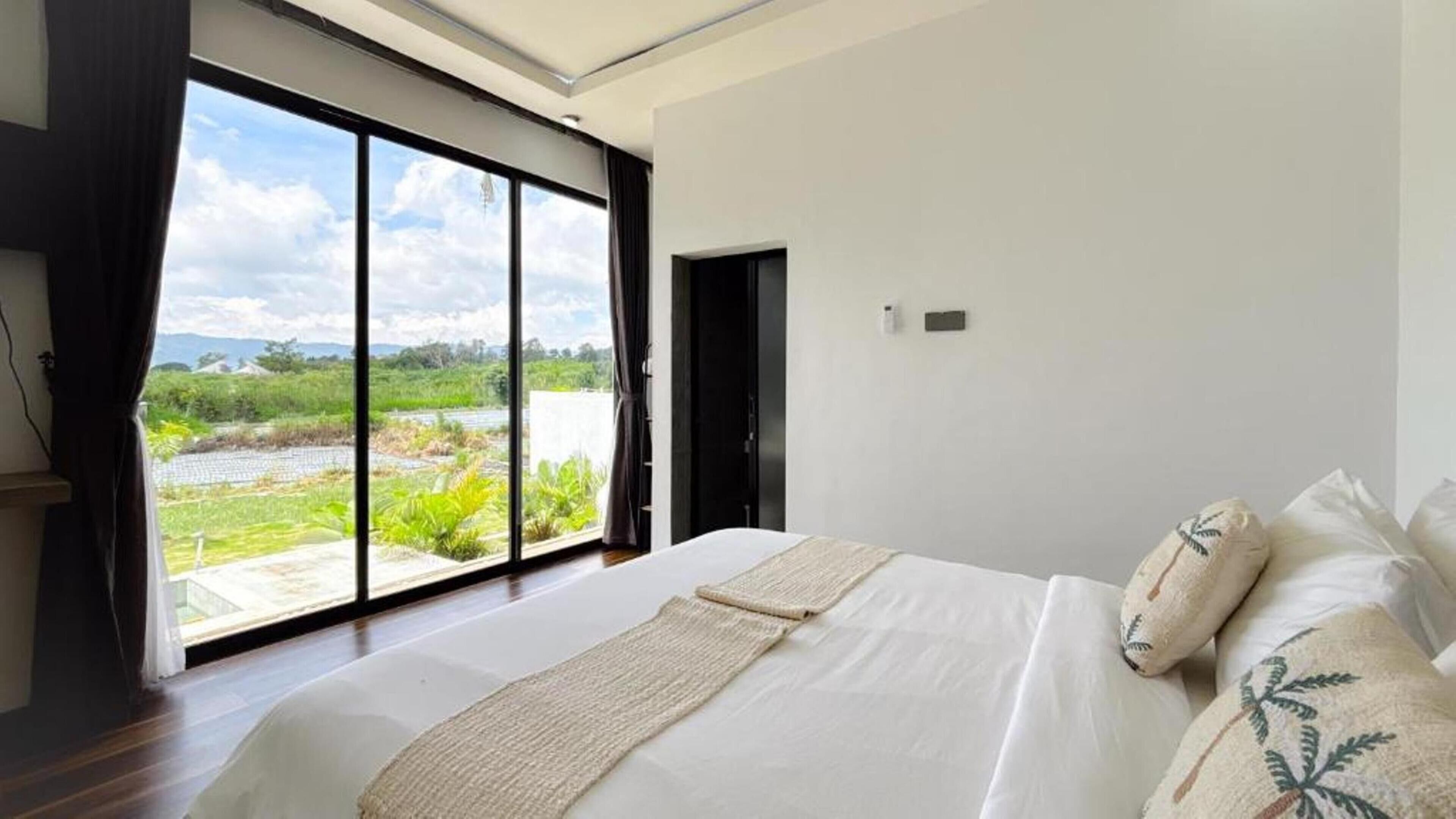 Ein Schlafzimmer mit einem großen Bett, Blick auf Grünflächen und ein Gewässer, sowie einer Schiebetür, die in einen anderen Raum führt.