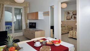 Un comedor con una mesa dispuesta para el desayuno, un televisor y vistas de un dormitorio con cama y cortinas.