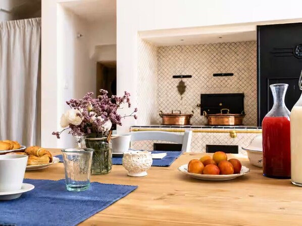 A breakfast table with pastries, a fruit plate, a vase with flowers, a glass, and a bottle.