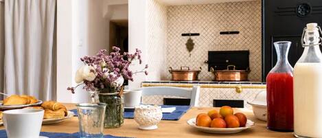 A breakfast setting with croissants, a glass of water, a vase with flowers, a plate of oranges, and a milk bottle.