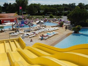 Un parque acuático con un tobogán amarillo grande, múltiples piscinas y tumbonas.
