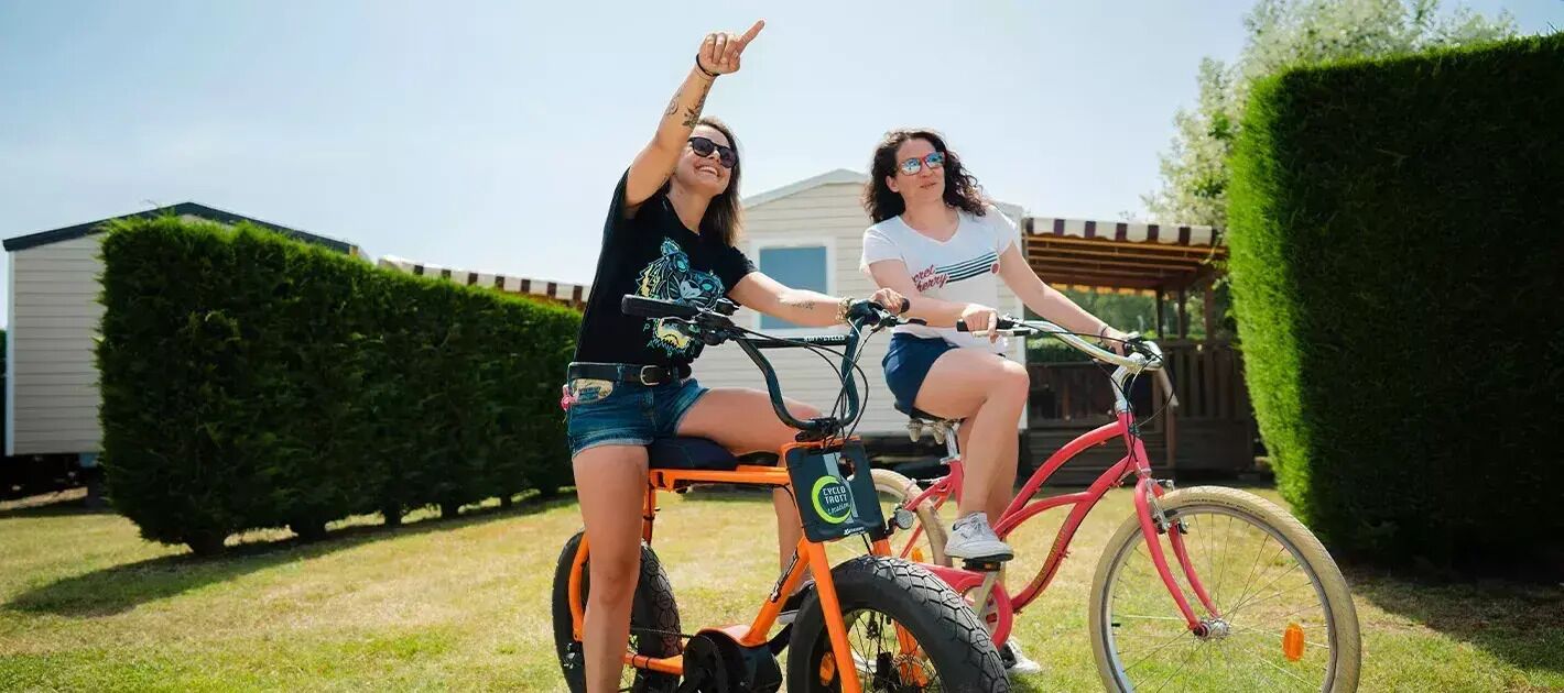 Dos personas en bicicletas eléctricas en un patio trasero, con una casa y setos al fondo.