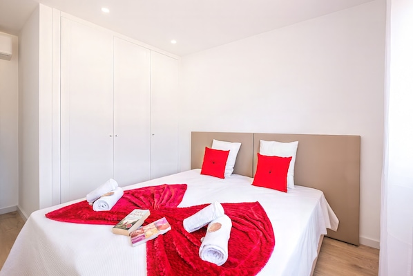 A hotel room with a large bed, white and red bedding, a wooden headboard, and a wardrobe. - Apartment with pool near beach in Albufeira (Albufeira)