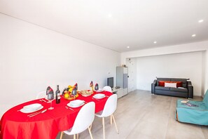 Ein Essbereich mit rotem Tischlein, weißen Stühlen und einem grauen Sofa im Hintergrund.