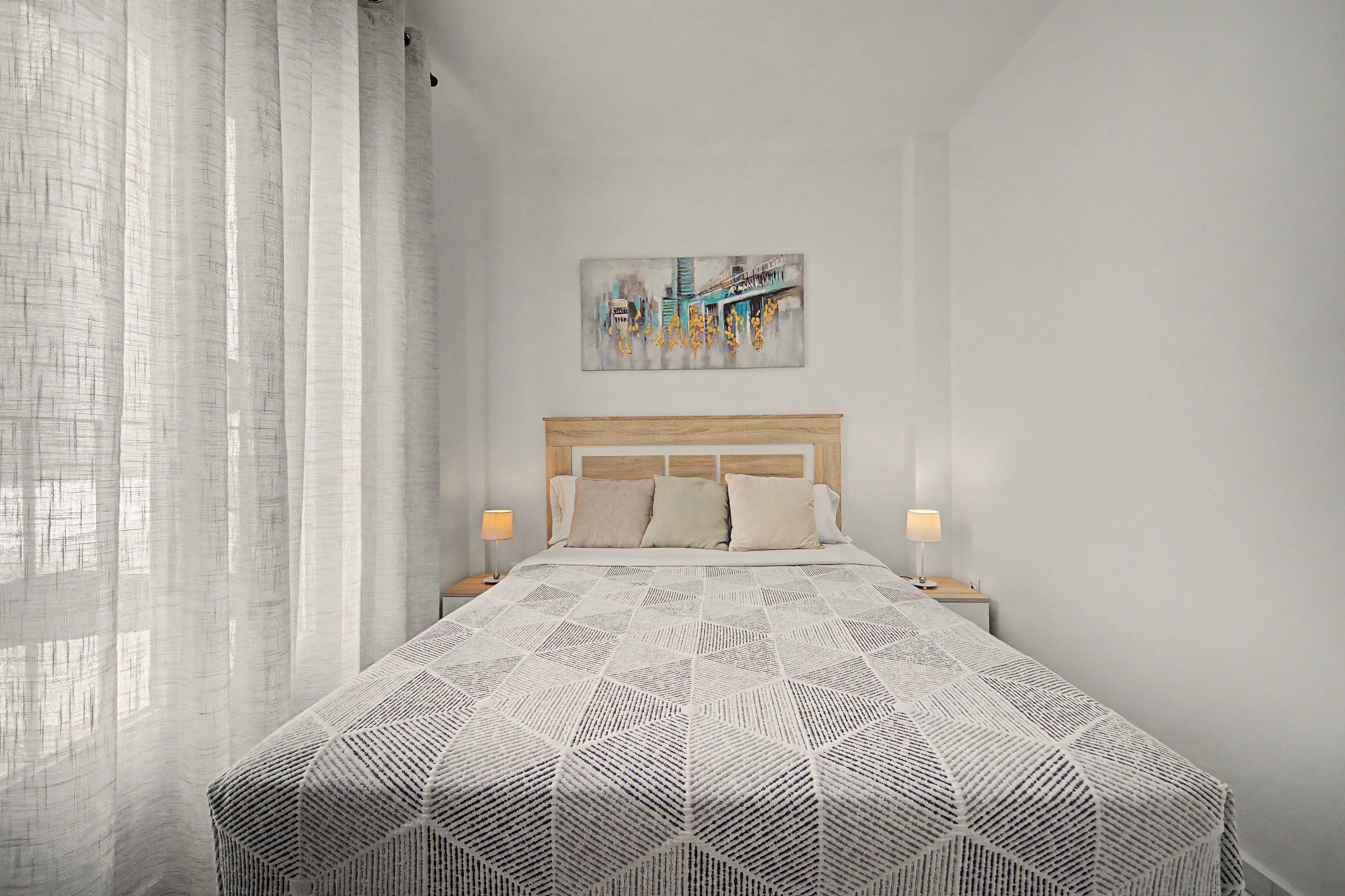 Une chambre d’hôtel bien aménagée, avec un grand lit, deux lampes de chevet, une tête de lit et un tableau accroché au mur.