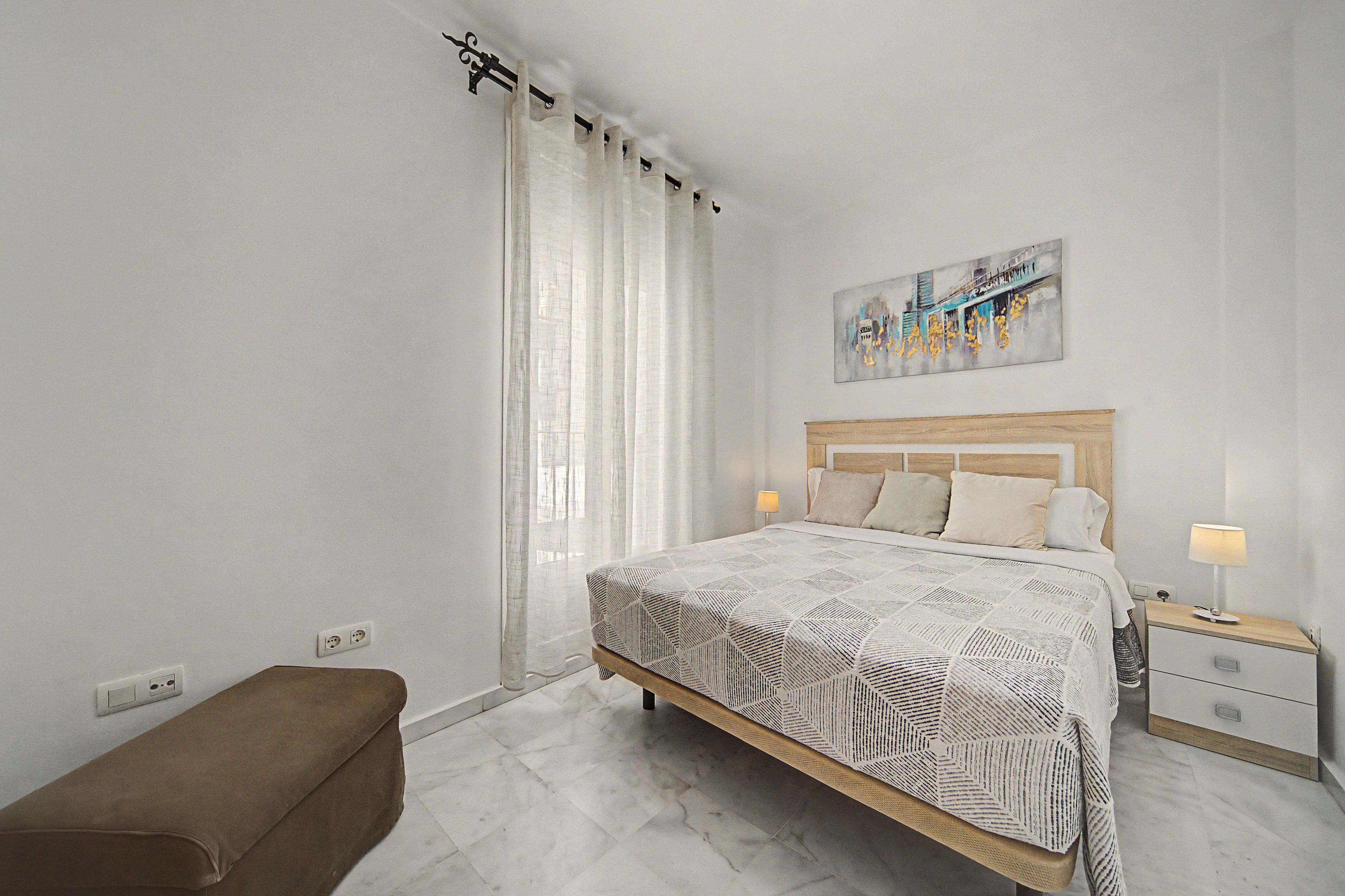 Une chambre à coucher moderne avec un lit, des tables de chevet, un banc et un tableau au mur.