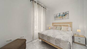 Une chambre à coucher moderne avec un lit, des tables de chevet, un banc et un tableau au mur.