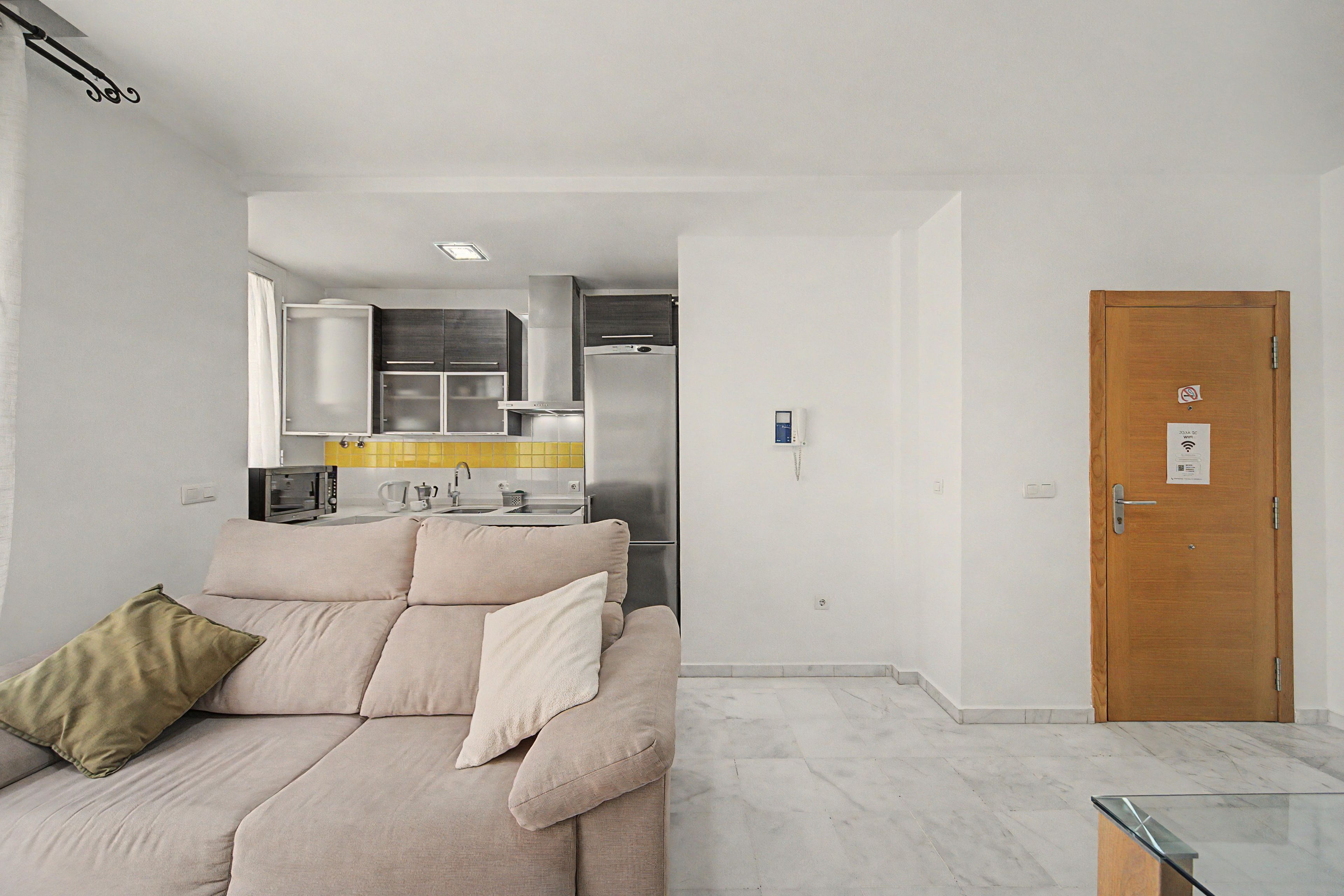 A modern living room with a sofa, a wooden door, and a kitchen area in the background.