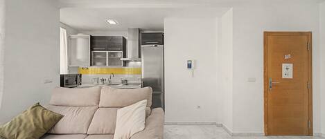 A modern living room with a sofa, a wooden door, and a kitchen area in the background.