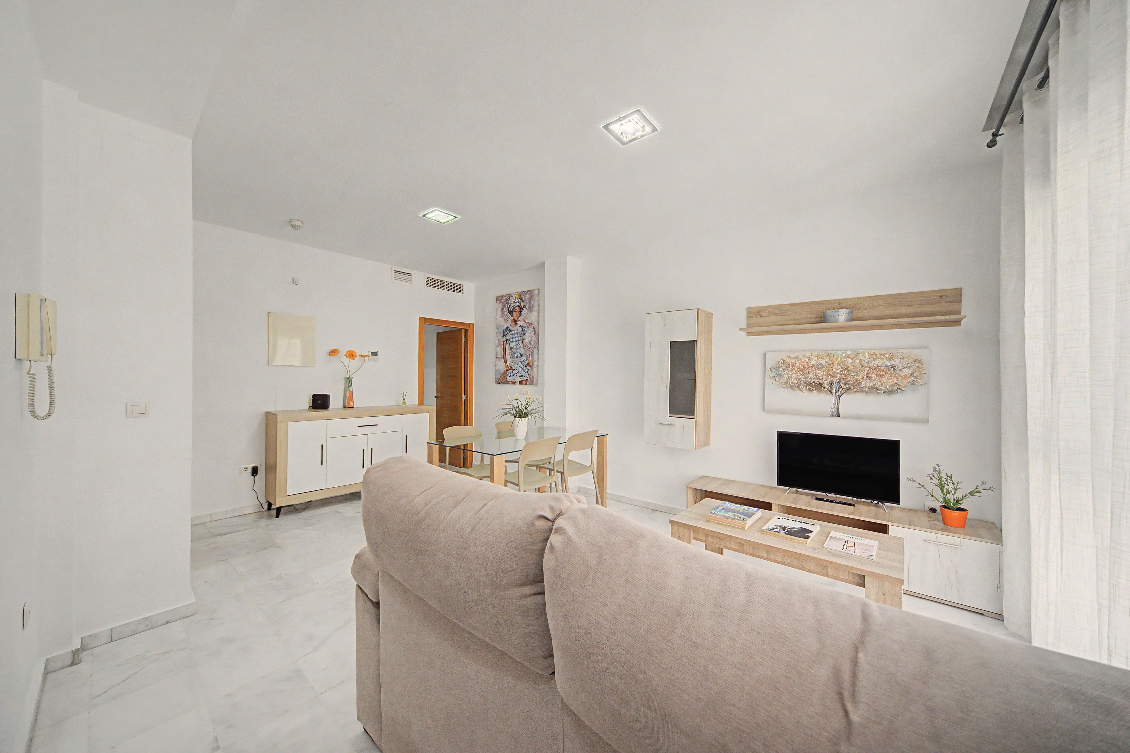 Un soggiorno moderno con divano, tavolino, televisore e zona pranzo con sedie e credenza.