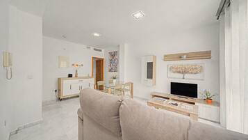 Un salon moderne comprenant un canapé, une table basse, un téléviseur et un coin repas avec des chaises et un buffet.