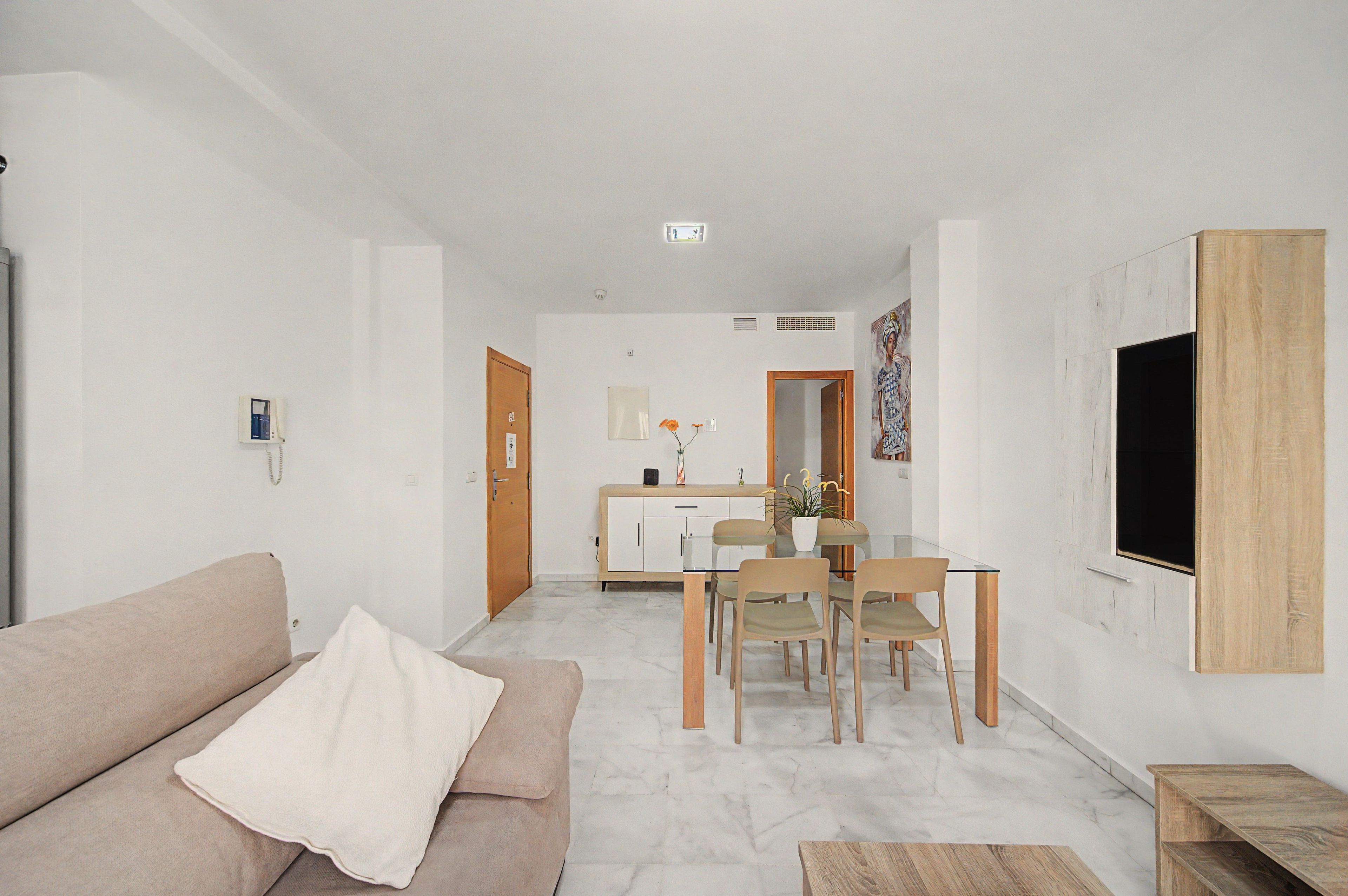A modern living room with a sofa, a dining table with chairs, and a TV mounted on the wall.