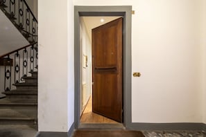 A wooden door with a brass handle, a staircase with black metal railings, and a small rug at the bottom of the stairs. - Cavalleggeri Palace - 3-Bedroom Apartment (Firenze)