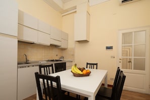 A compact kitchen with white cabinets, a dining table with chairs, and a fruit basket on the table. - Cavalleggeri Palace - 3-Bedroom Apartment (Firenze)