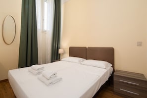 Ein Hotelzimmer mit Bett, Nachttisch, Lampe und einem Fenster mit Vorhängen.