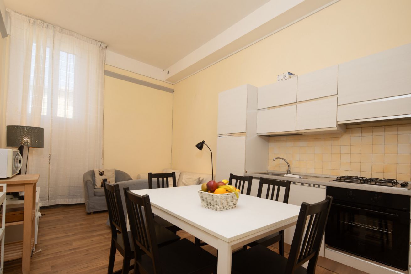 Une cuisine compacte comprenant une table à manger, des chaises, un four à micro-ondes, une cuisinière et un panier de fruits.