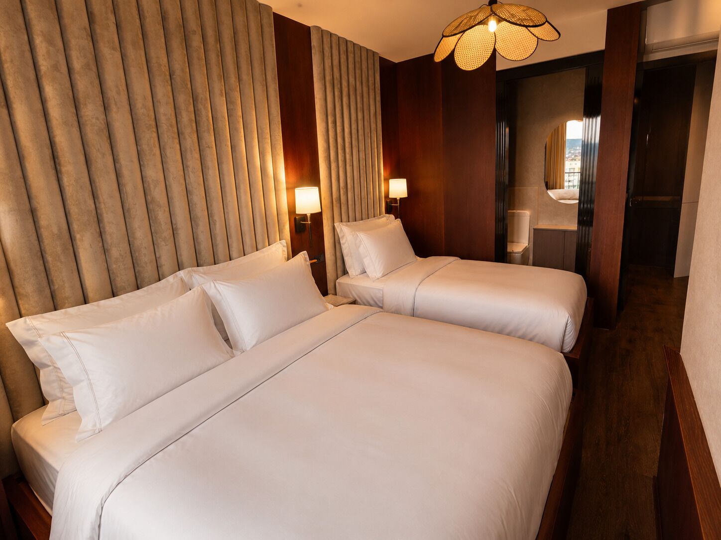 A hotel room with two beds, a wooden headboard, and a modern lamp.